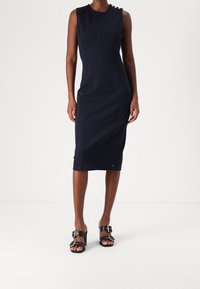Granatowa, bezrękawnikowa sukienka o dopasowanym kroju, z guzikami na ramionach i pionowymi szwami, zestawiona z czarnymi sandałami na klamry.