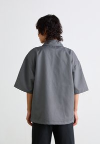 Gray short-sleeve shirt with a relaxed fit, featuring a soft texture and a stand collar. Minimalist design with no visible patterns or hardware.