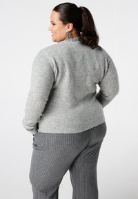 Grijze gebreide trui met een ronde hals en textuurelementen, gecombineerd met grijze pantalon met krijtstreep. De stof ziet er zacht en comfortabel uit.