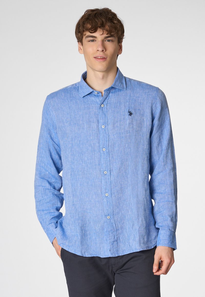 Camicia azzurro chiaro a maniche lunghe con bottone in tessuto testurizzato, dotata di colletto, chiusura frontale con bottoni e un piccolo logo scuro sul lato sinistro del petto.