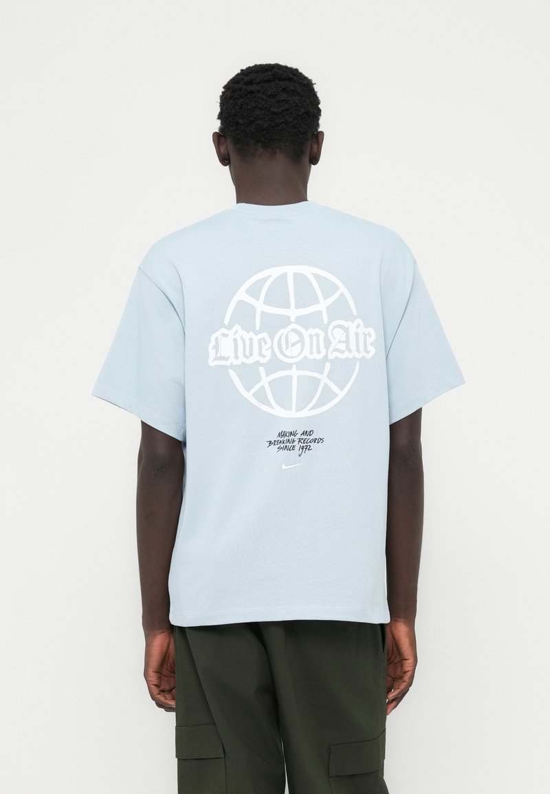 Ανοιχτό μπλε βαμβακερό μπλουζάκι με μεγάλο λευκό γραφικό της γης και το κείμενο «Live On Air» στην πλάτη. Κοντά μανίκια, άνετη εφαρμογή.