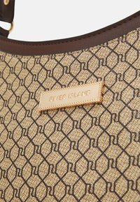Nærbillede af en beige mønsterhandtaske med brune detaljer og en gylden "River Island" mærkeplade.