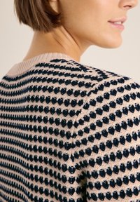 Gebreide trui met een textuurpatroon in marineblauw en crème kleuren; heeft een ronde halslijn en ribgebreide accenten op de kraag.