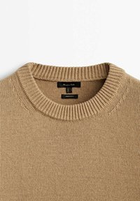 Pull beige en maille à col rond avec col côtelé et étiquettes de marque noires à l'intérieur de l'encolure.