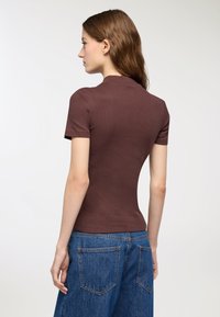 Top corto a maniche corte marrone a coste, con silhouette aderente, colletto alto e texture liscia, abbinato a jeans in denim blu a vita alta.