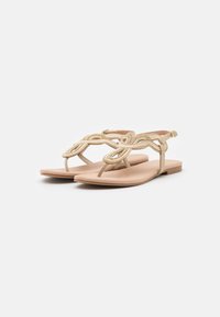 Platta sandaler med en beige konstläderöverkant, som har dekorativa vävda remmar och en smidig, flexibel sula. Justerbar ankelrem ingår.