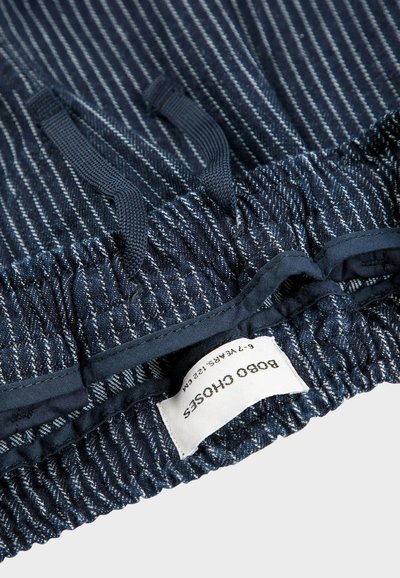 Marina tygshorts med vita randningar, elastisk midja med justerbara snören och en etikett som visar storleksinformation.