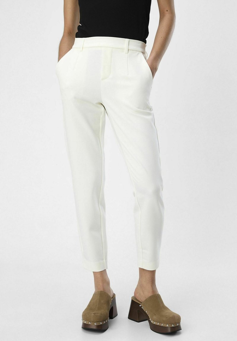 Pantalones blancos ajustados de tela estructurada, con bolsillos laterales, un corte entallado y un acabado suave, combinados con zuecos marrones.