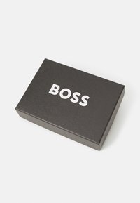 Zwarte rechthoekige doos met een gladde textuur, voorzien van vetgedrukte witte "BOSS" letters op de bovenkant.