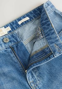 Jean en denim bleu à coupe décontractée. Doté d'un zip, d'un bouton en métal et d'un tissu à motifs à l'intérieur de la ceinture. Design classique à cinq poches.