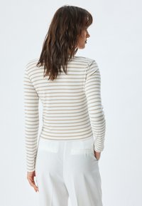 Langsleeve top in crèmekleur met verticale beige strepen, gemaakt van een zachte stof. Slim fit met een ronde halslijn; gecombineerd met crèmekleurige broek.