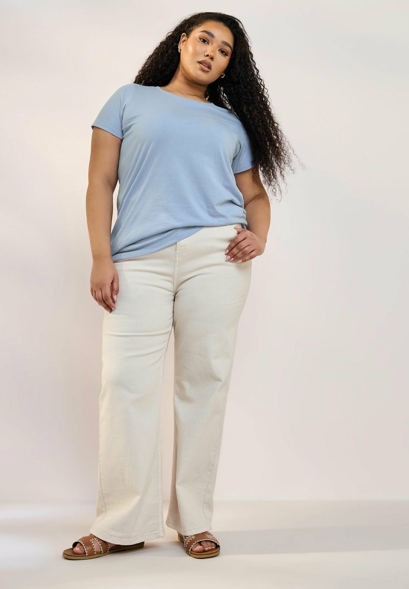 Ljusblå, kortärmad t-shirt kombinerad med krämfärgade vida byxor och bruna sandaler. Outfiten har en avslappnad passform och mjuka texturer.