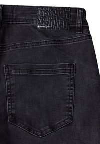 Poche arrière d’un jean en denim noir avec des détails cousus et une étiquette de marque noire texturée portant la mention « Street One » sur la ceinture.