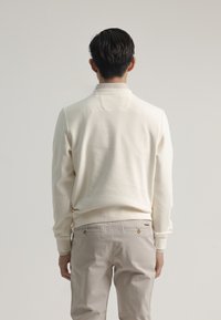 Sudadera de color crema en tejido texturizado con cuello, puños acanalados y dobladillo. Combinada con pantalones de beige claro con dos bolsillos traseros.