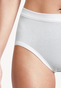 Primo piano dei fianchi e della vita di una persona che indossa biancheria intima bianca in cotone semplice con elastico in vita su uno sfondo bianco.