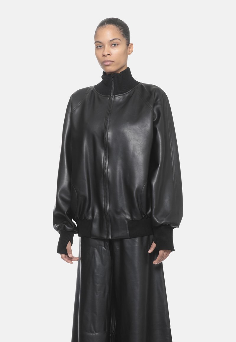 Giubbotto bomber in pelle nera con colletto e polsini a costine. Presenta una vestibilità comoda e chiusura con zip. Texture liscia e finitura lucida.