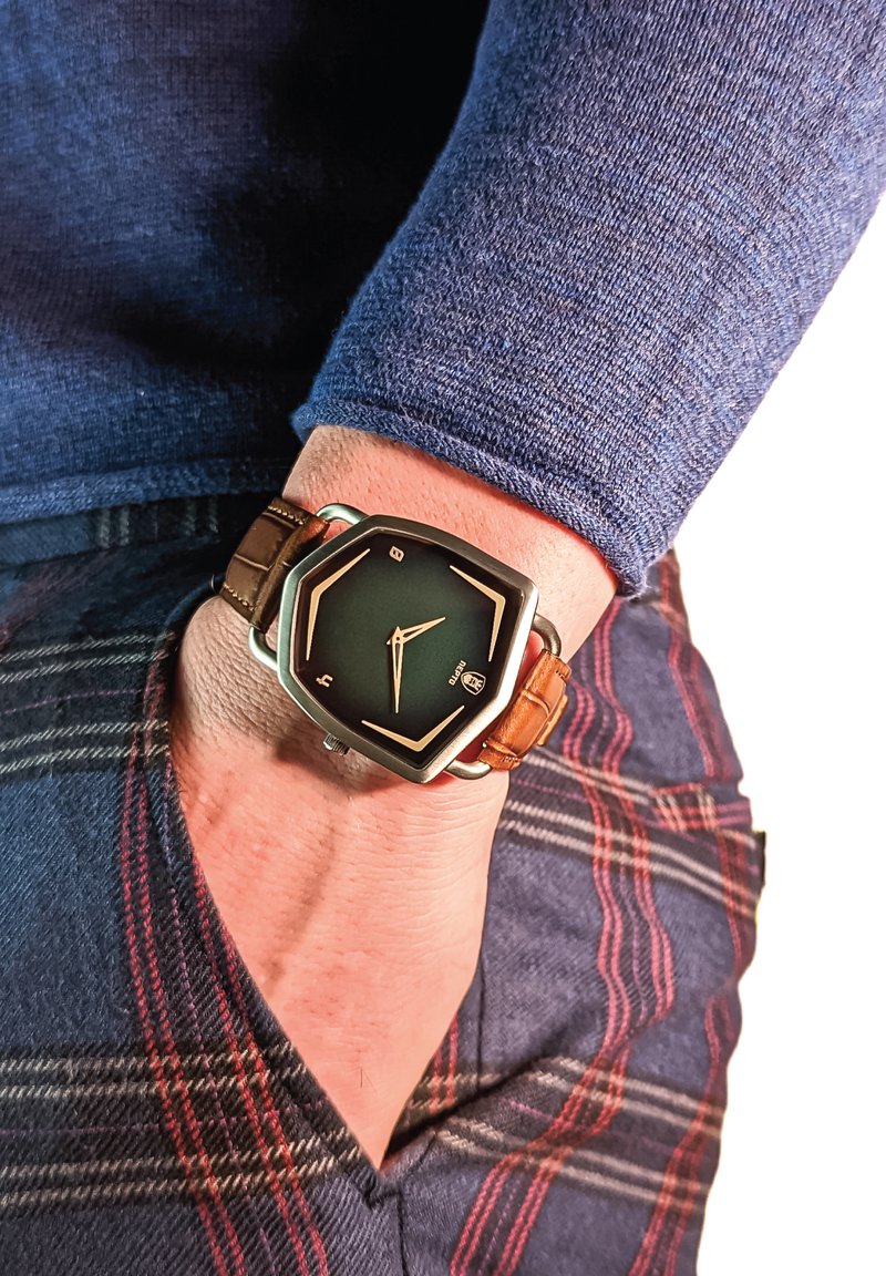 Hexagonal ansigt ur med en sort urskive og guld detaljer. Brun læderrem, placeret på et håndled, med ternet stof synligt i baggrunden.