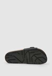 Svart gummisula med ett strukturerat greppmönster, som har en beige korkfotbädd och ett svart justerbart rem för en säker passform.