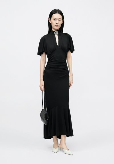 Fekete ruha testhezálló felsőrésszel, rövid lebegő ujjakkal és bővülő szegéllyel. Kulcslyuk alakú nyílással és a nyaknál díszítő brossal rendelkezik.