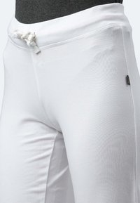 Weiße Baumwoll-Sweatpants mit einem breiten Bund und Kordelzug. Glatte Textur, enganliegendes Design und ein Etikett auf der linken Seite.