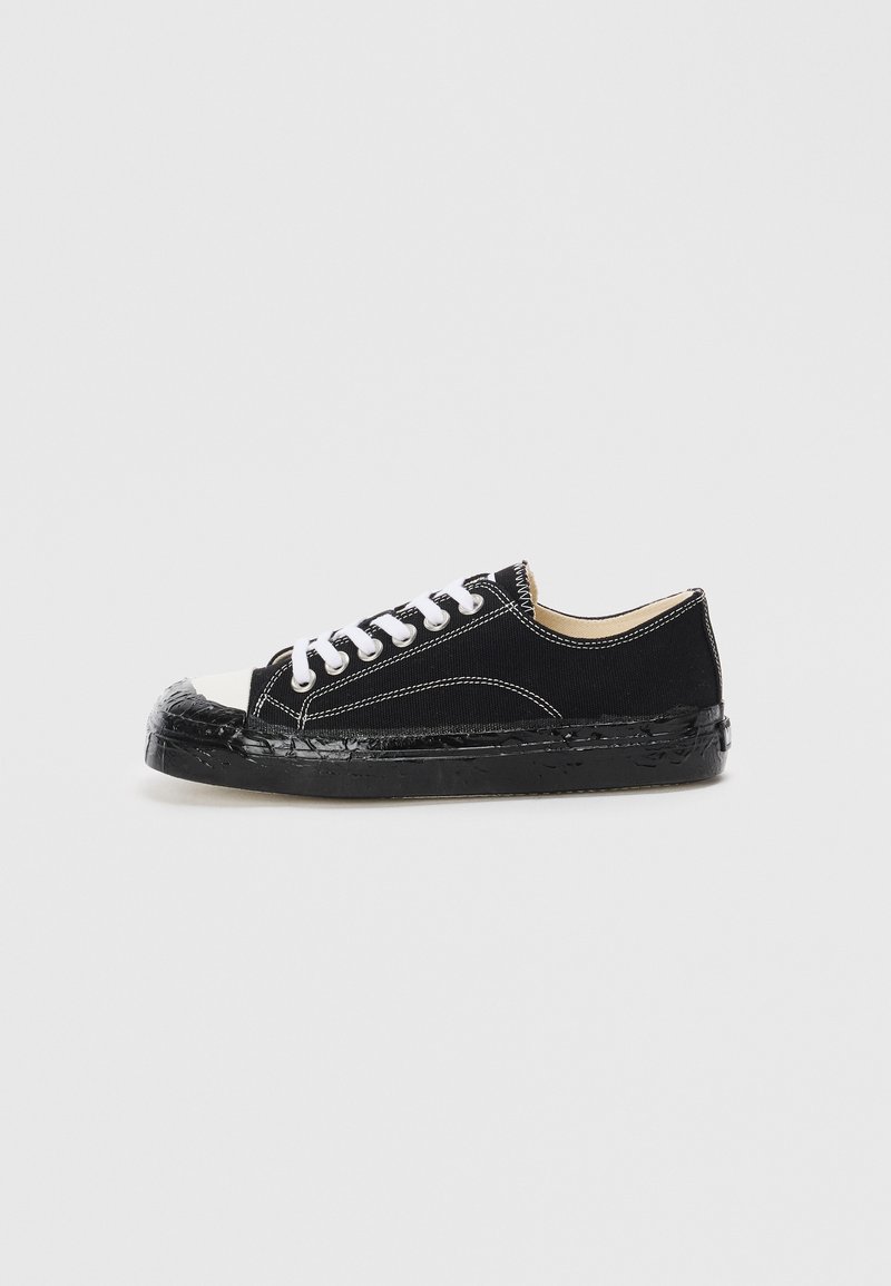 Black canvas sneakers with white laces, rubber toe cap, and textured black sole. Features white stitching and a low-cut design.