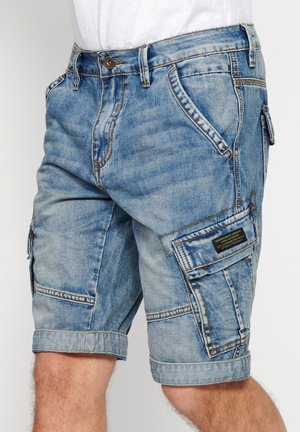 Pantalones cortos de mezclilla azul claro con un corte relajado, múltiples bolsillos y puños enrollados. Presentan costuras en contraste y una etiqueta en el bolsillo lateral.