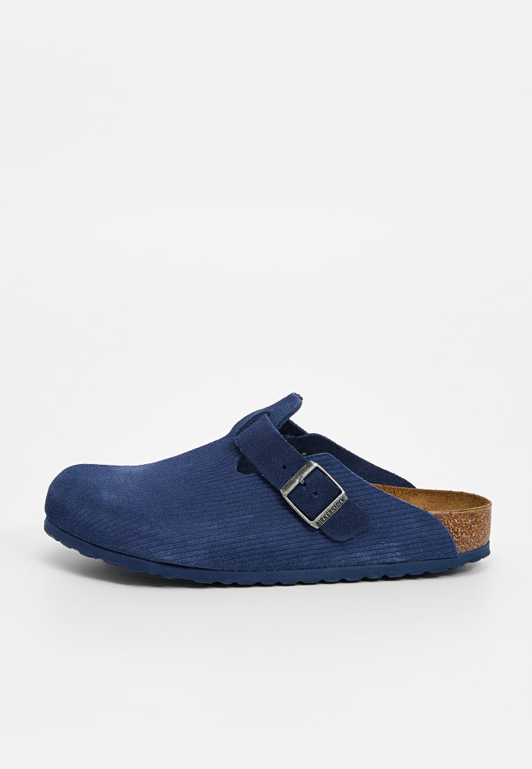Navyblaue Wildlederschläppchen mit strukturiertem Obermaterial, verstellbarem Metallverschluss und Korkfußbett. Runde Zehenpartie und flache Gummisohle.