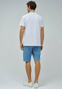 Camiseta de algodón blanca combinada con pantalones cortos de mezclilla azul claro. Los pantalones cortos tienen un corte clásico con bolsillos traseros y un dobladillo limpio.