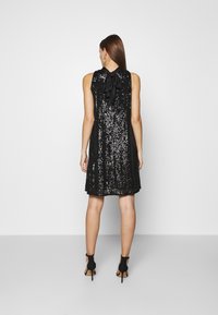 Czarna sukienka z cekinami o luźnym kroju, z kokardą na plecach i bez rękawów. Noszona z wysokimi sandałami.