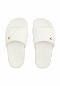 Chanclas blancas con un upper texturizado, que presentan un acento de logo dorado. Las suelas son planas y ligeramente acolchadas para mayor comodidad.