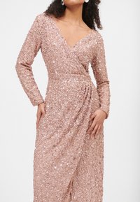 Różowa sukienka z koralikami, z długimi rękawami, dekoltem w kształcie litery V i marszczonym detalem w talii. Posiada obfite błyszczące cekiny oraz swobodną sylwetkę.