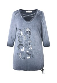 Harmaa pitkähihainen tunika, jossa on V-kaula-aukko. Käytännöllinen, painettu kuvio hopeisilla yksityiskohdilla ja naruhelma, joka mahdollistaa säädettävän istuvuuden.