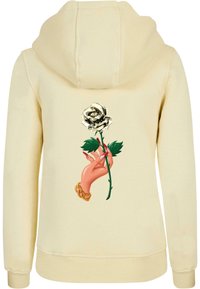 Felpa color crema con una grande grafica di una mano che tiene una rosa bianca. Il design presenta foglie verdi e un accento di catena dorata.