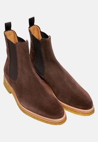 Hnědé semišové Chelsea boty s elastickými bočními panely, zaoblenými špičkami a béžovými gumovými podrážkami s prošívaným okrajem.