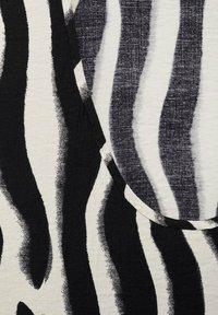 Zwart-witte stof met brede zebra-stripes. De textuur lijkt zacht met een lichte glans, wat het gedurfde ontwerp versterkt.