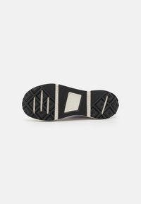 Sole di scarpa in gomma nera con motivo di grip testurizzato, una sezione centrale di colore chiaro e tre prominenti scanalature orizzontali per migliorare la trazione.