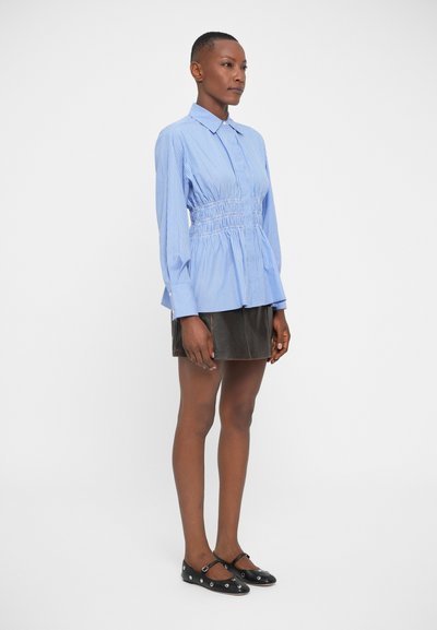 Camicia button-up a righe blu e bianche con vita cinchata e maniche lunghe, abbinata a una gonna in pelle nera e scarpe basse nere.