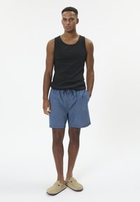 Top nero, pantaloni corti a righe blu con coulisse, e pantofole beige. L'outfit presenta un design semplice e una vestibilità confortevole.