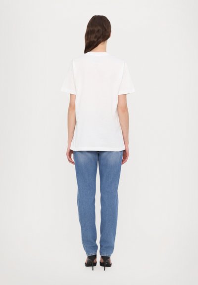Vit kortärmad t-shirt med rund halsringning, kombinerad med ljusblå raka jeans och svarta högklackade skor.