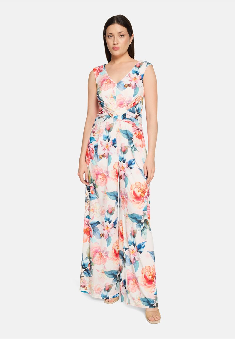 Combinaison florale avec un col en V, de courtes manches cape et une taille ceinturée. Le tissu présente des motifs floraux colorés rose et bleu sur un fond blanc.