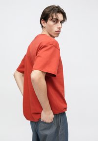 Κόκκινο βαμβακερό T-shirt με κοντά μανίκια, άνετη εφαρμογή και στρογγυλή λαιμόκοψη. Το ύφασμα φαίνεται λείο, με διακριτική λάμψη και χωρίς ορατά σχέδια.