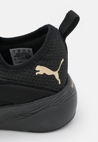 Chaussure de sport noire avec une tige en mesh texturé, un talon arrondi et un logo Puma doré sur le côté ; équipée d'une languette pour un enfilage facile.
