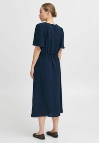 Navy blue midi dress with short puff sleeves, elastic waist, back button closure, and textured dotted pattern throughout. Flat black shoes.