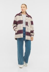 Cămașă oversized în carouri, crem, burgund și bleumarin. Are un sistem de închidere cu nasturi și buzunare mari, asortată cu blugi cu talie înaltă și adidași albi.