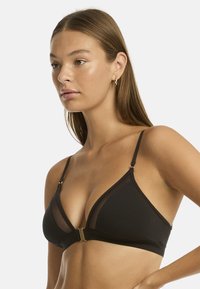 Reggiseno triangolare nero con pannelli trasparenti e dettagli in tonalità oro. Tessuto morbido e spalline regolabili per migliorare la vestibilità e il comfort.