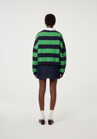 Groene en marineblauwe gestreepte sweatshirt, oversized pasvorm, met een witte kraag; gecombineerd met een donkere denim rok en accessoires, gezien vanuit de achterkant.