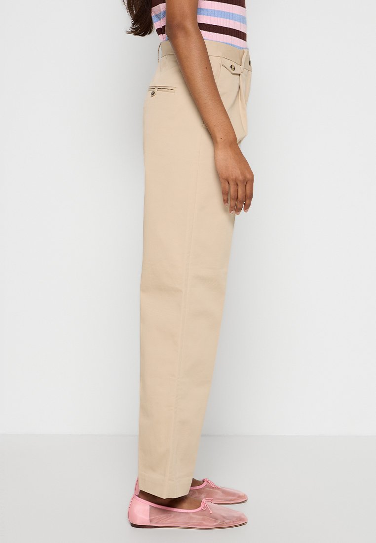 Pantaloni beige a vita alta con gamba dritta, dalla texture liscia, tasche frontali e una leggera piega; abbinati a ballerine rosa.