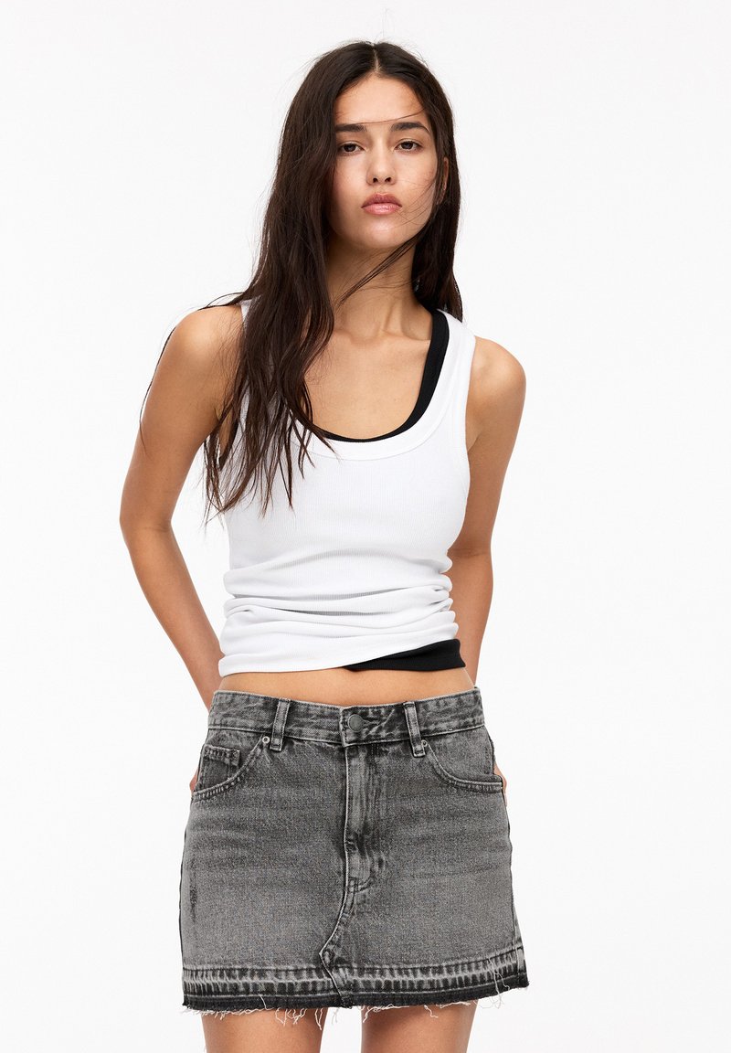 Witte geribbelde tanktop over een zwarte tanktop, gecombineerd met een grijze denimrok met een rafelig zoom en een klassieke 5-pocket ontwerp.