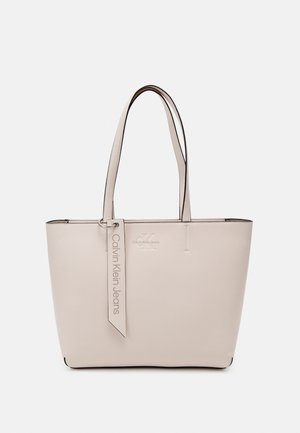 Sac cabas beige Calvin Klein Jeans avec deux longues anses et une étiquette suspendue portant le nom de la marque.