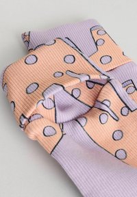 Multifarvede rørstrikkede sokker med et lavendel- og ferskenmønster og store sorte prikker. Stoffet ser blødt og strækbart ud.